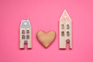 Decorative heart between two house models on pink background